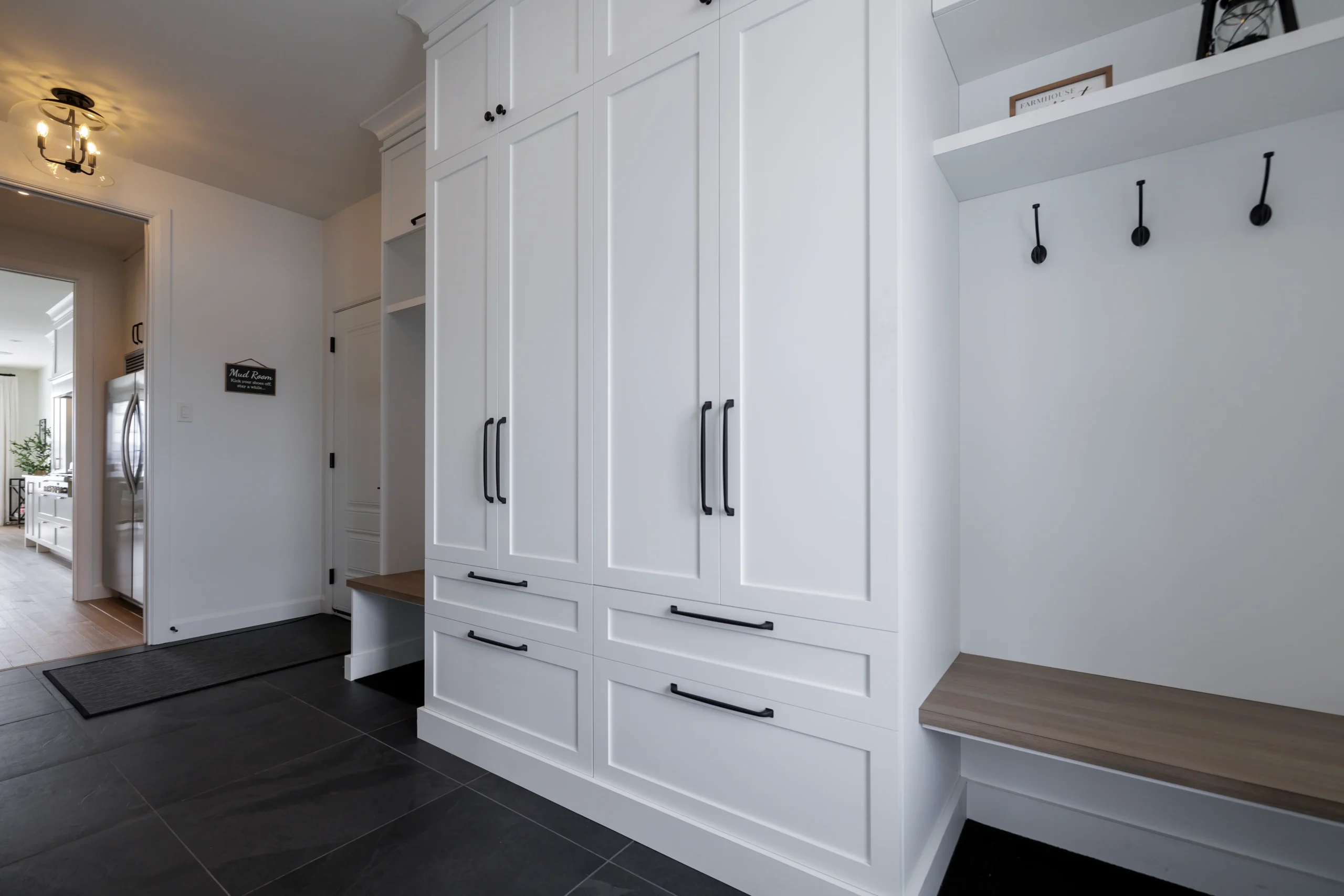 Grande armoire d’entrée sur mesure blanche avec banc intégré, crochets muraux et rangements fermés.