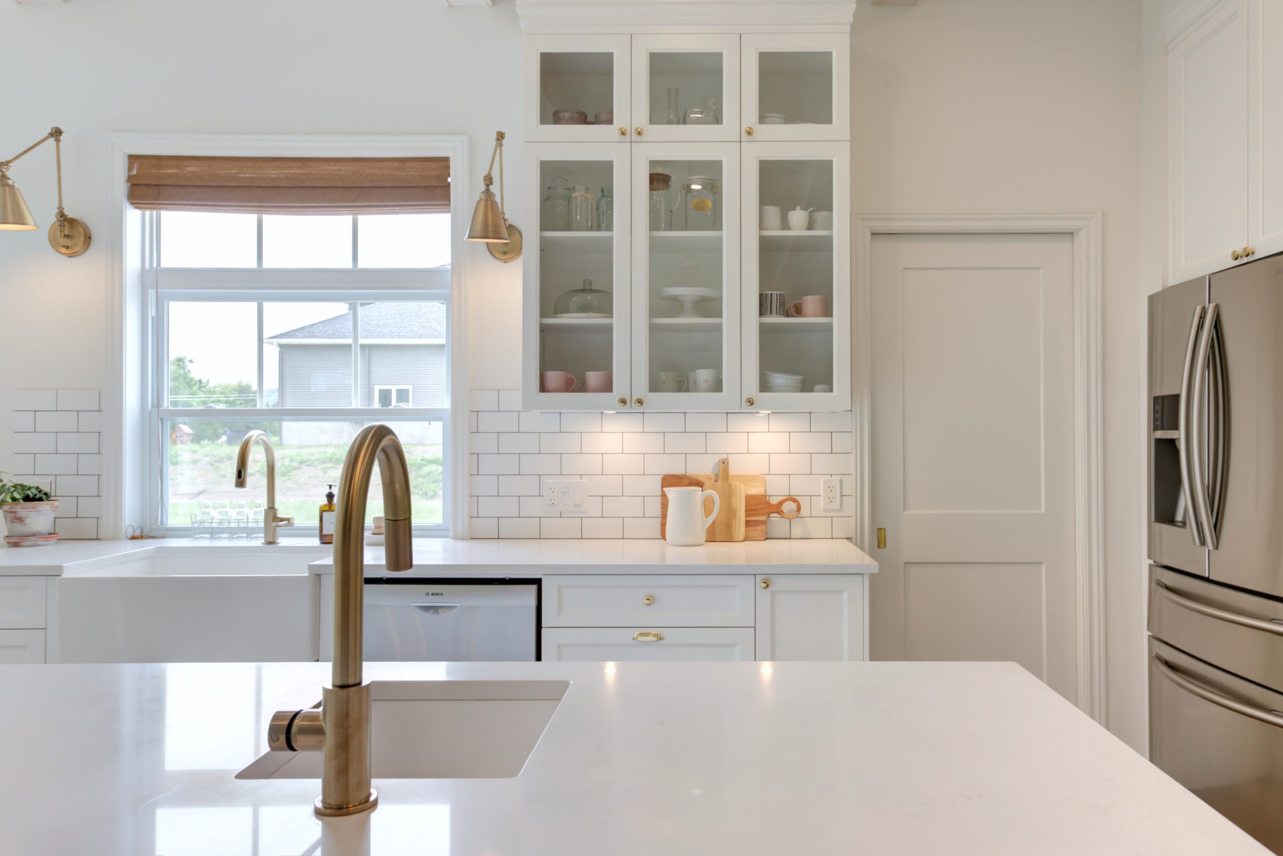 White kitchen island with integrated sink and gold faucet in a bright, classic and minimalist kitchen.