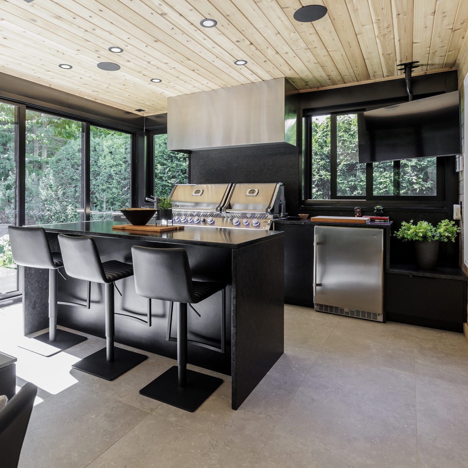 Modern kitchen with black island featuring an integrated cooktop, black stools and large windows overlooking a lush garden.