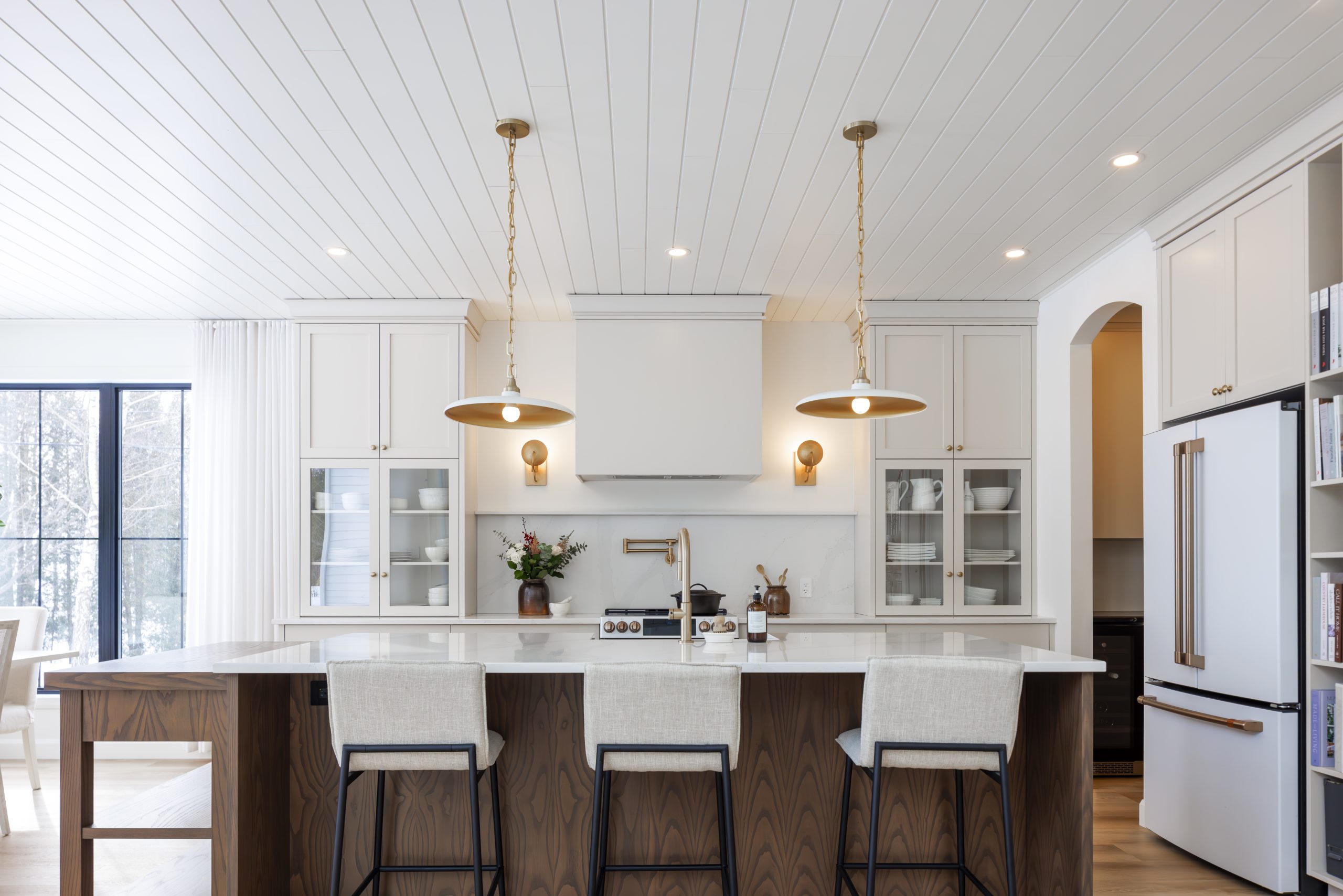 Large bright kitchen with a white island, upholstered stools, cream cabinets and elegant gold pendant lighting.