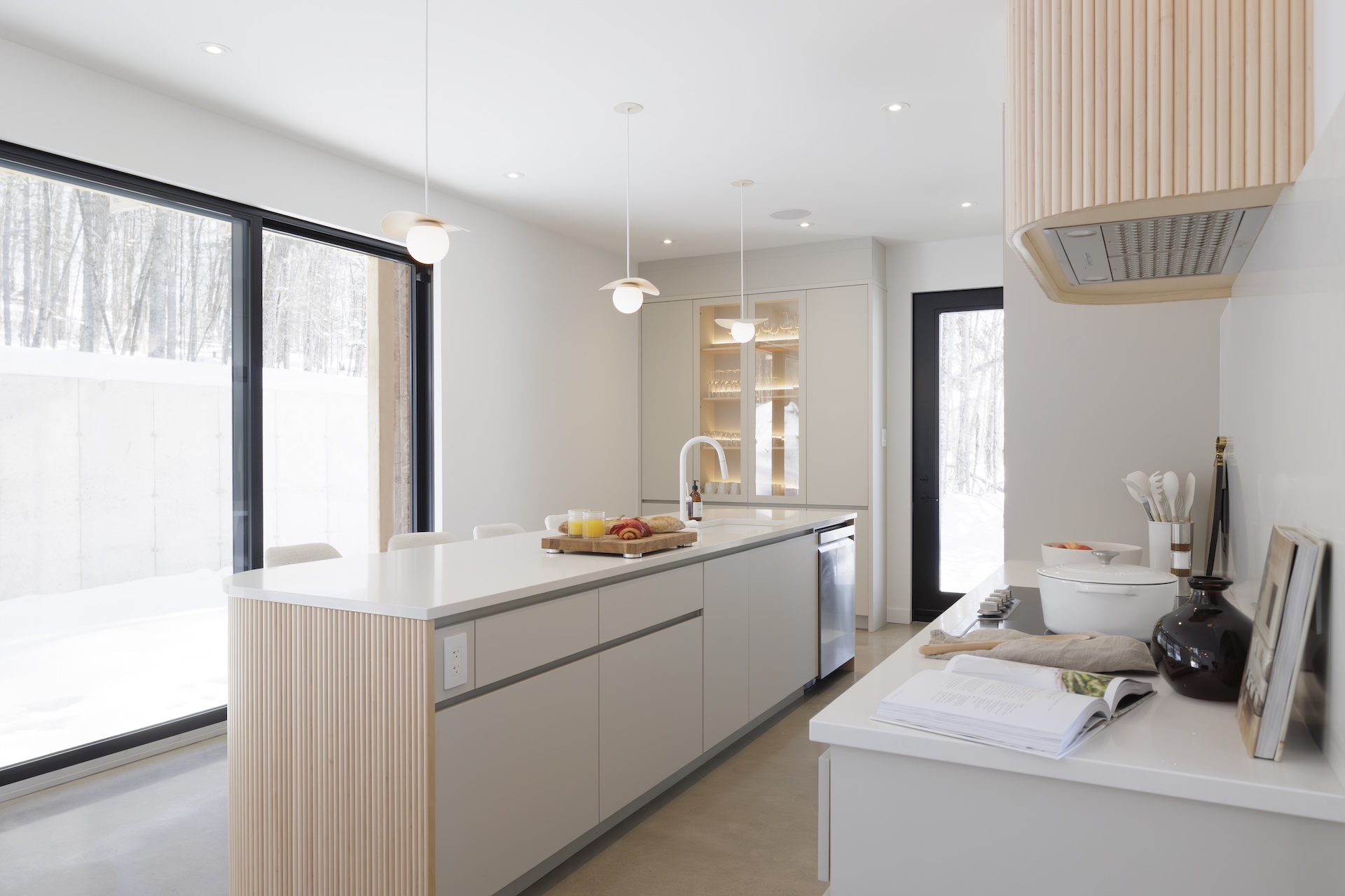 Preparation island with light finish in a bright modern kitchen featuring large black-framed windows and a spacious work surface.