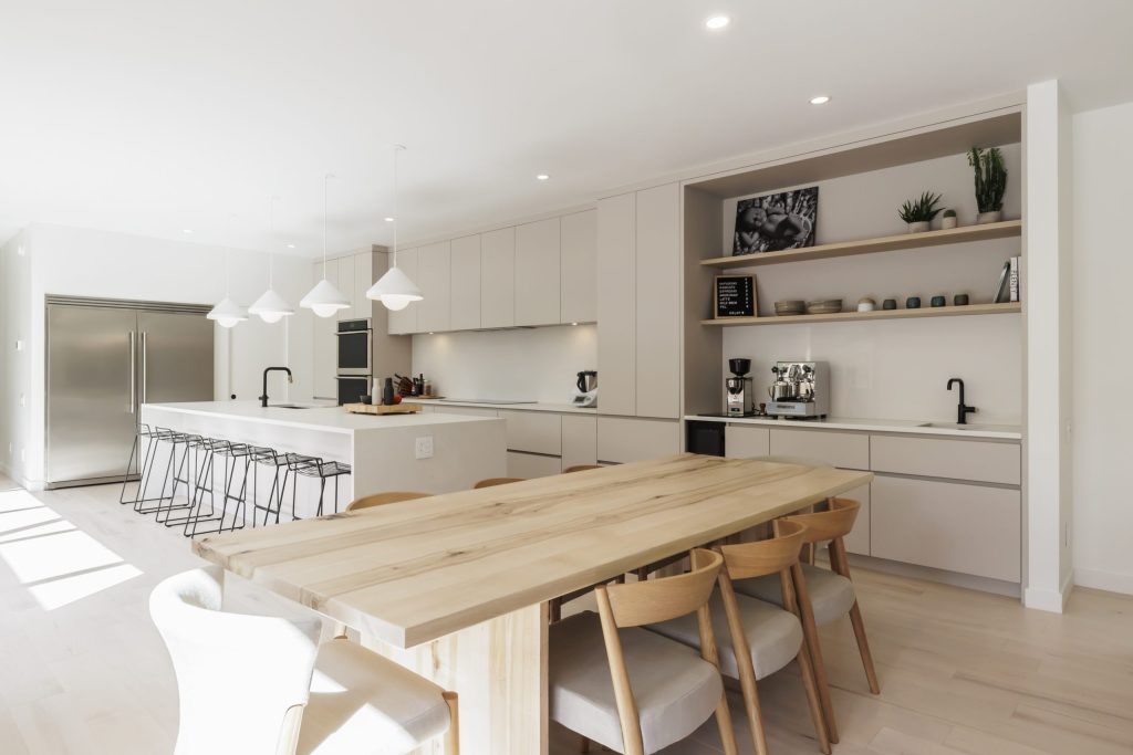 Cuisine moderne avec îlot blanc, grandes étagères ouvertes et table en bois clair | Modern kitchen with white island, large open shelves and light wood dining table