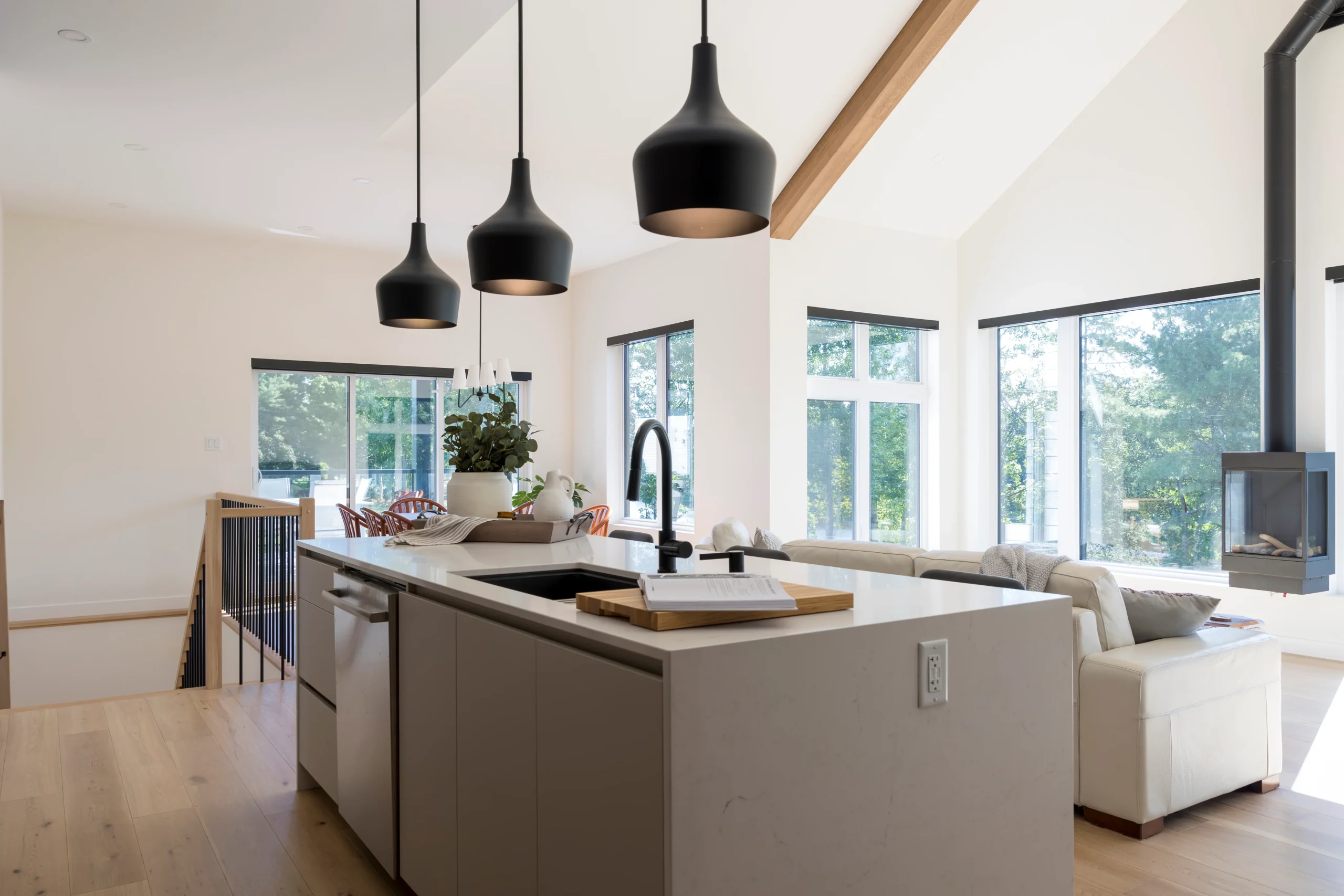 Contemporary kitchen with a white quartz island, black faucet and black pendant lights above a counter opening onto a bright living area.