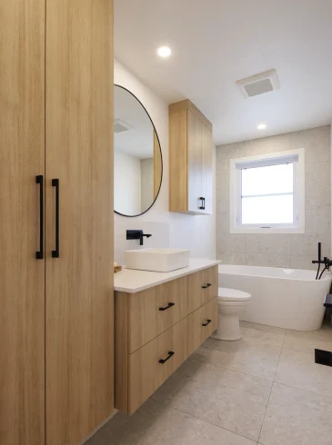 Salle de bain lumineuse avec meuble-lavabo flottant en bois clair, double vasque blanche et grand miroir rond | Bright bathroom with floating light wood vanity, double white sink and large round mirror