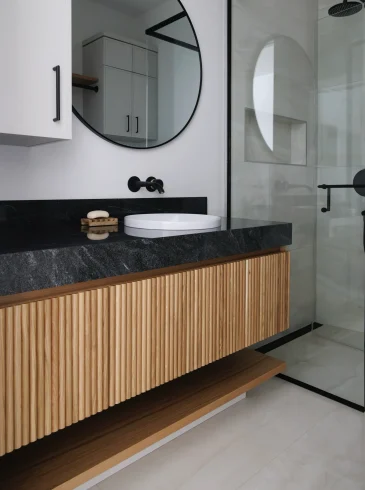 Armoire de salle de bain moderne avec façade en lattes verticales de bois et comptoir noir mat, design minimaliste | Modern bathroom vanity with vertical wood slat front and matte black countertop, minimalist design