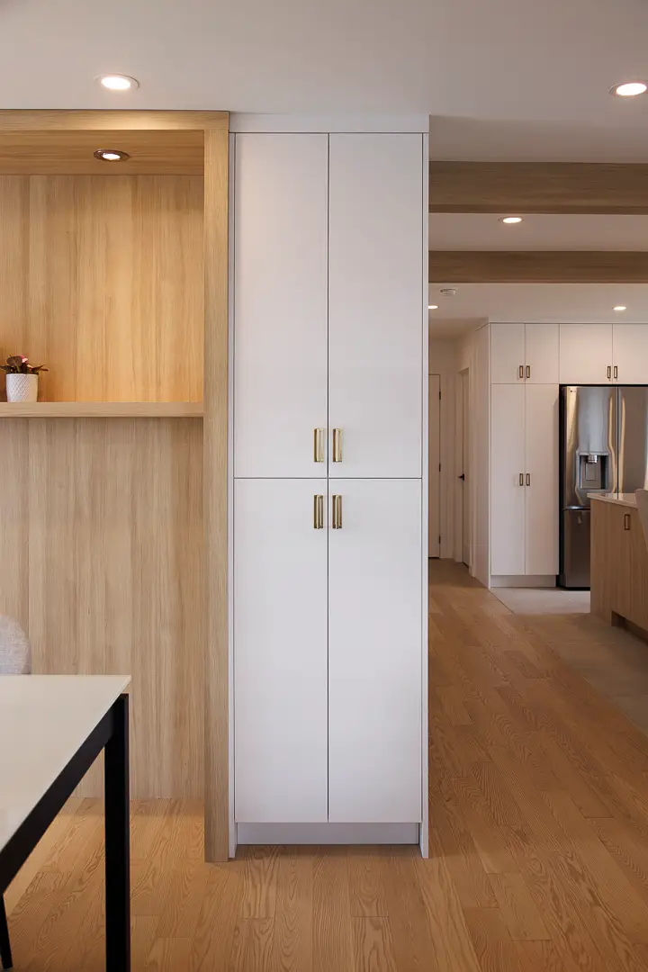 Custom storage cabinet in a modern entryway with white cabinets, gold handles and a lit wood alcove.