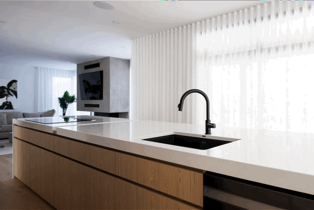 Contemporary large kitchen island with white countertop and matte black faucet, in a bright open space with minimalist lines.